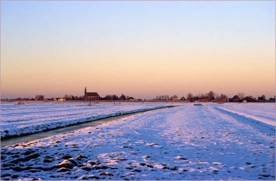 Oudendijk tegen zonsondergang, gezien van de brug in een besneeuwde Beetskoog