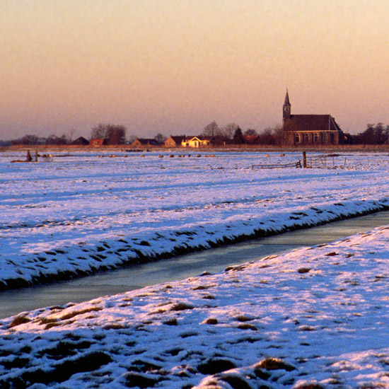 Zoom: Oudendijk tegen zonsondergang, gezien van de brug in een besneeuwde Beetskoog