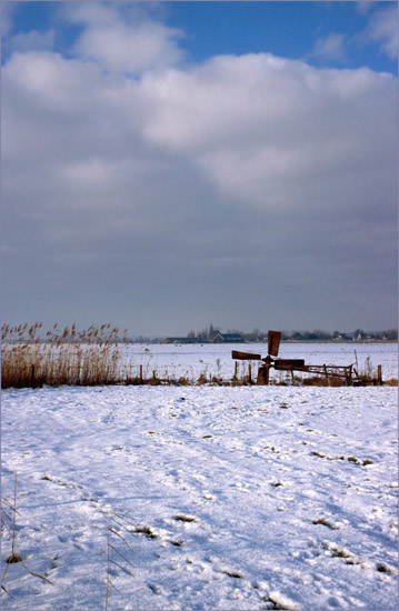 Oudendijk gezien over de sneeuw van de Beetskoog, met zieltogend molentje op de voorgrond