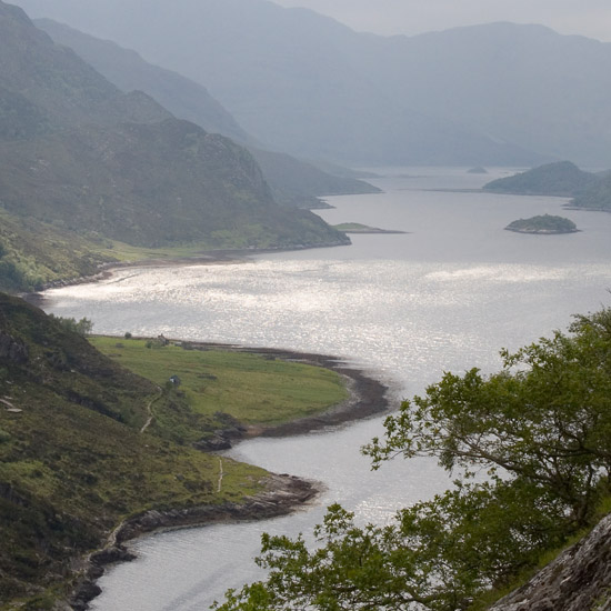 Zoom: Looking down on Skiary from the climb to Cadha Mhòr; bright sun breaks through dark clouds, lighting up Loch Hourn