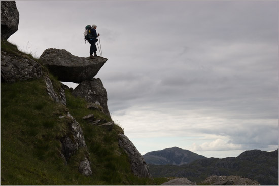 Lady with rucksack and camerabag watching evening clouds from a balancing rock on Meall nan Eun