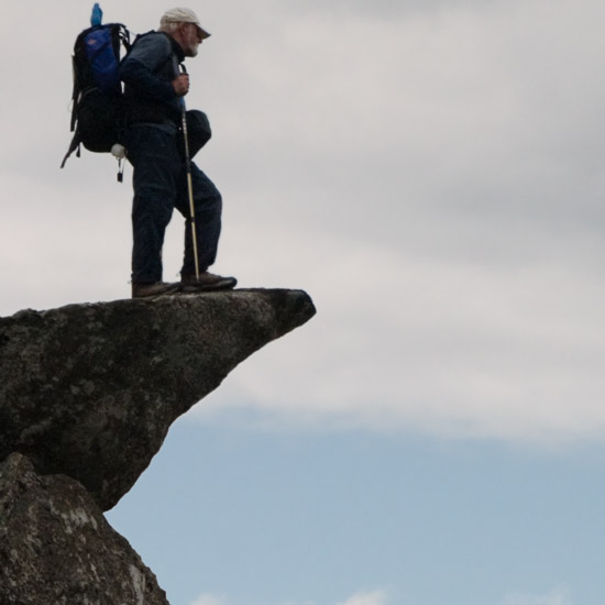 Zoom: Elderly gentleman with rucksack and camerabag watching evening clouds from Meall nan Eun